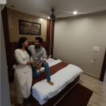 Couple relaxing in a clean and comfortable deluxe hotel room at Navodaya Sarovar, Orai, featuring modern interiors, cozy bedding, and a peaceful stay experience.